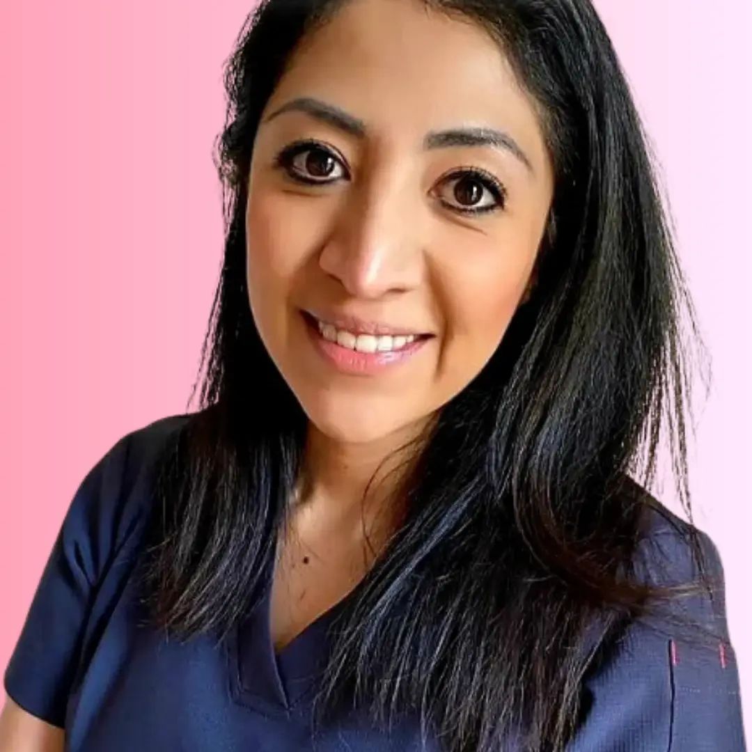 Bea Doula con uniforme azul marino sonriendo frente a fondo rosa, profesional en salud perinatal.