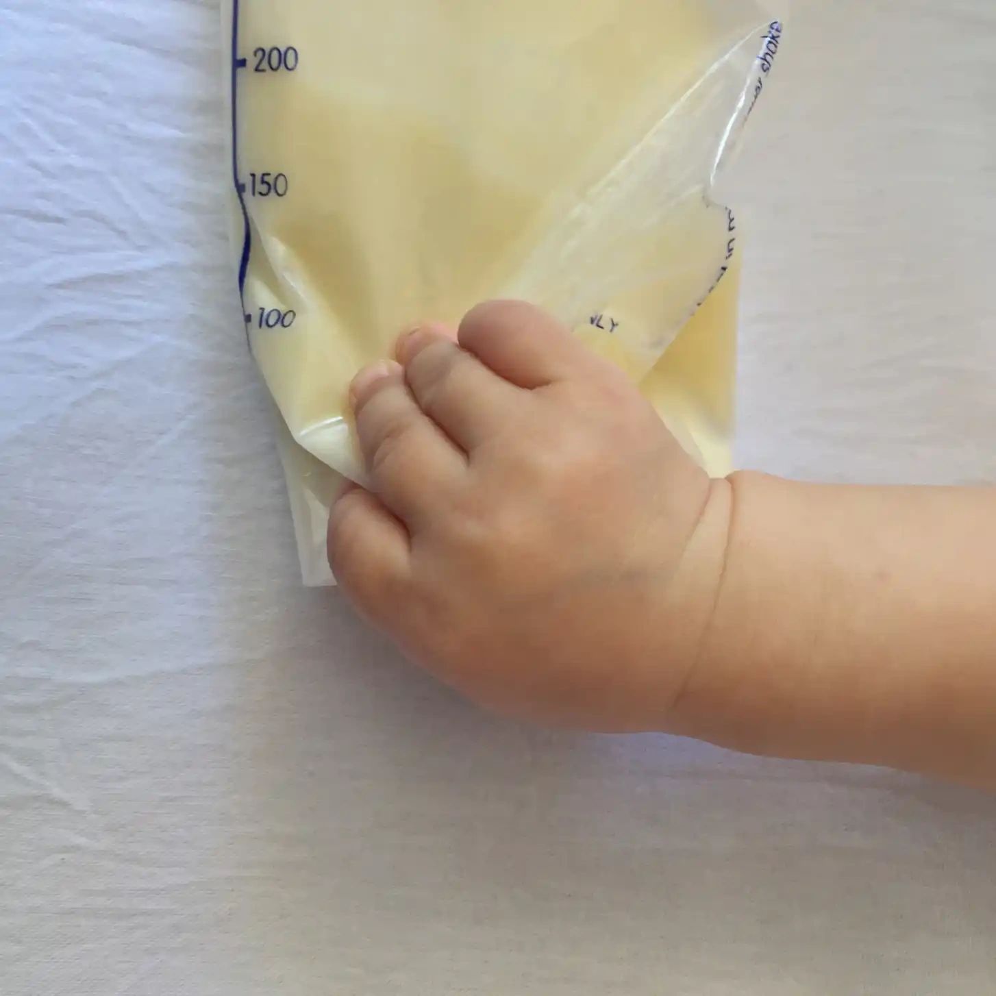 Mano de un bebé sobre una bolsa de leche materna almacenada con marcas de volumen